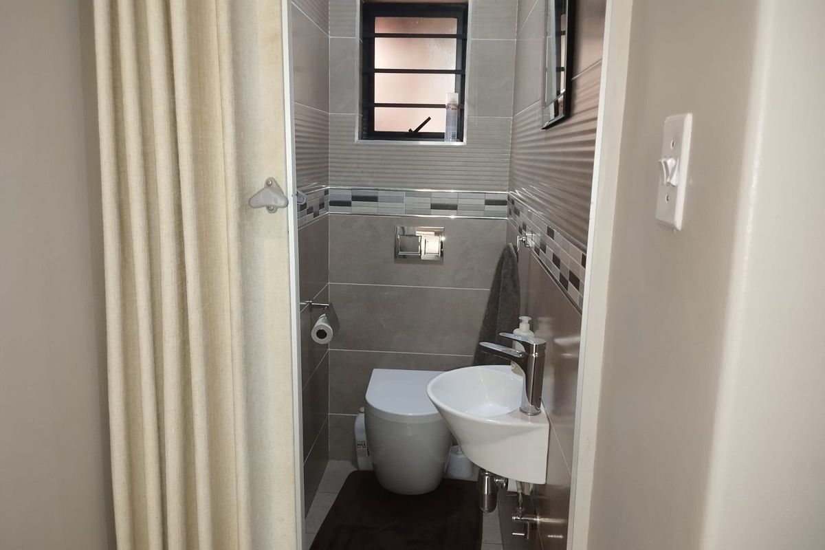 A compact, modern guest bathroom featuring a wall-mounted toilet, a small basin with a chrome mixer tap, and contemporary tiled wall finishes.