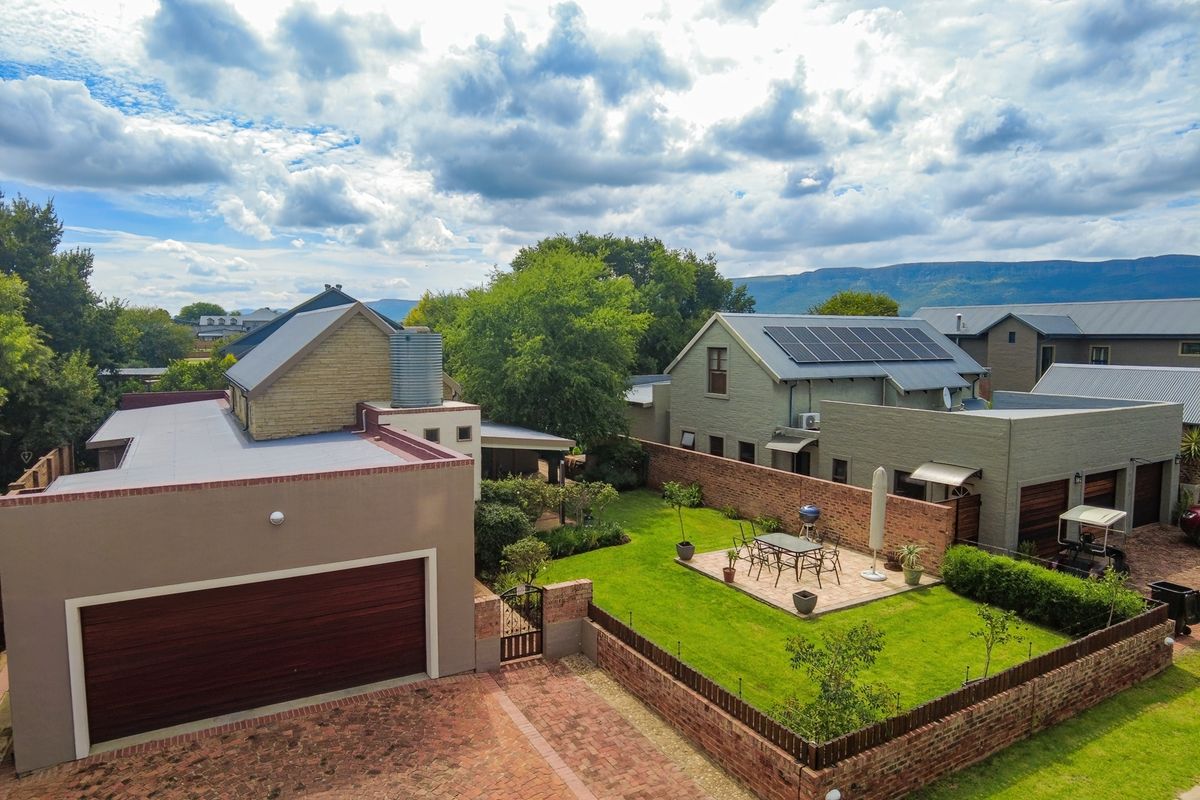 Aerial view of a residential property featuring a landscaped garden, paved patio area, brick boundary walls, and a house equipped with roof-mounted solar panels.
