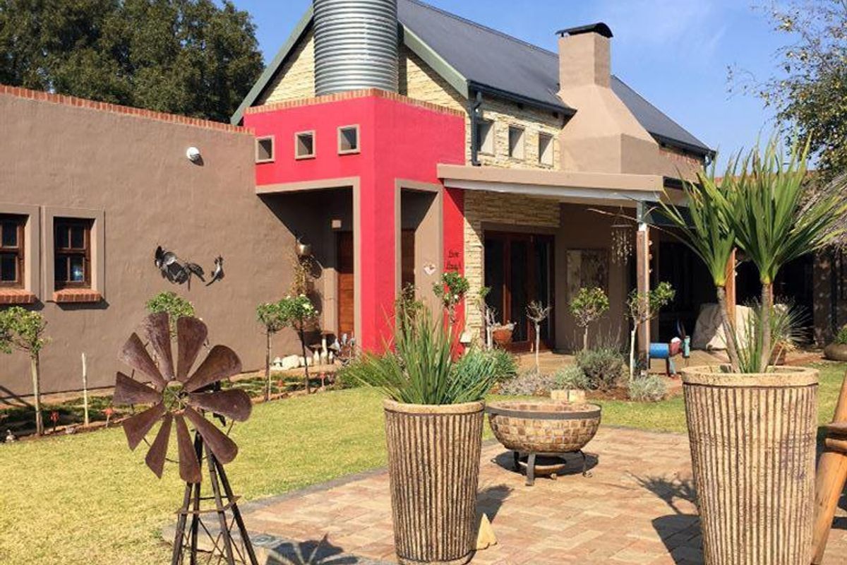 A rear view of the house featuring a paved patio area, stone cladding, a prominent water tank, and a chimney.