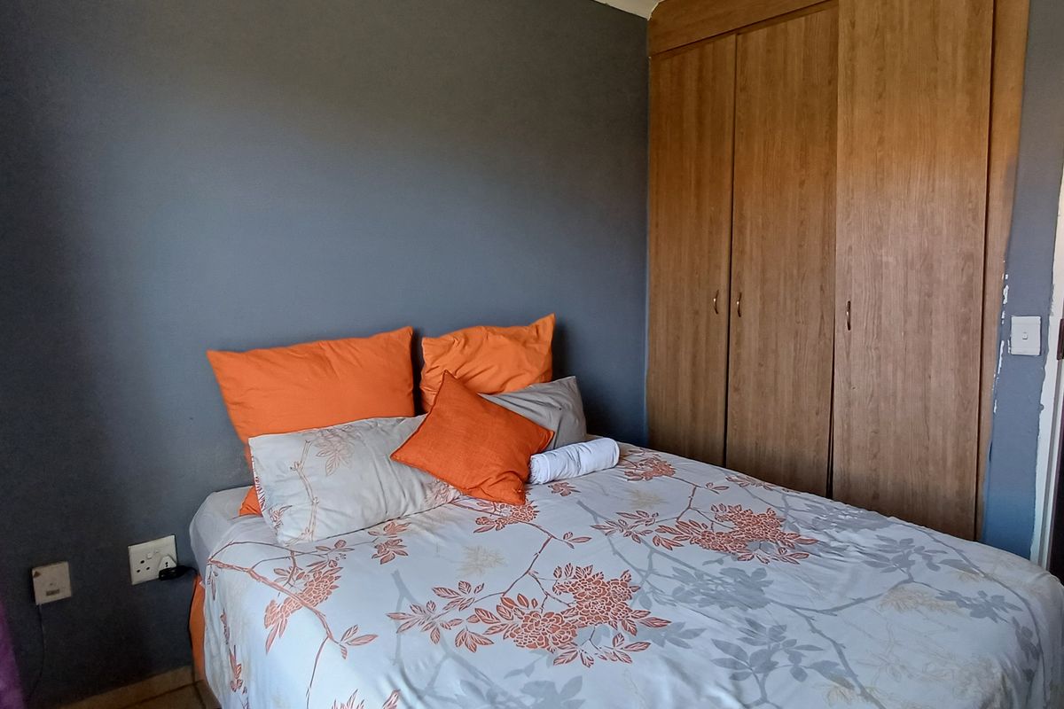 A bedroom featuring tiled flooring, a built-in wooden wardrobe, and a dark accent wall.