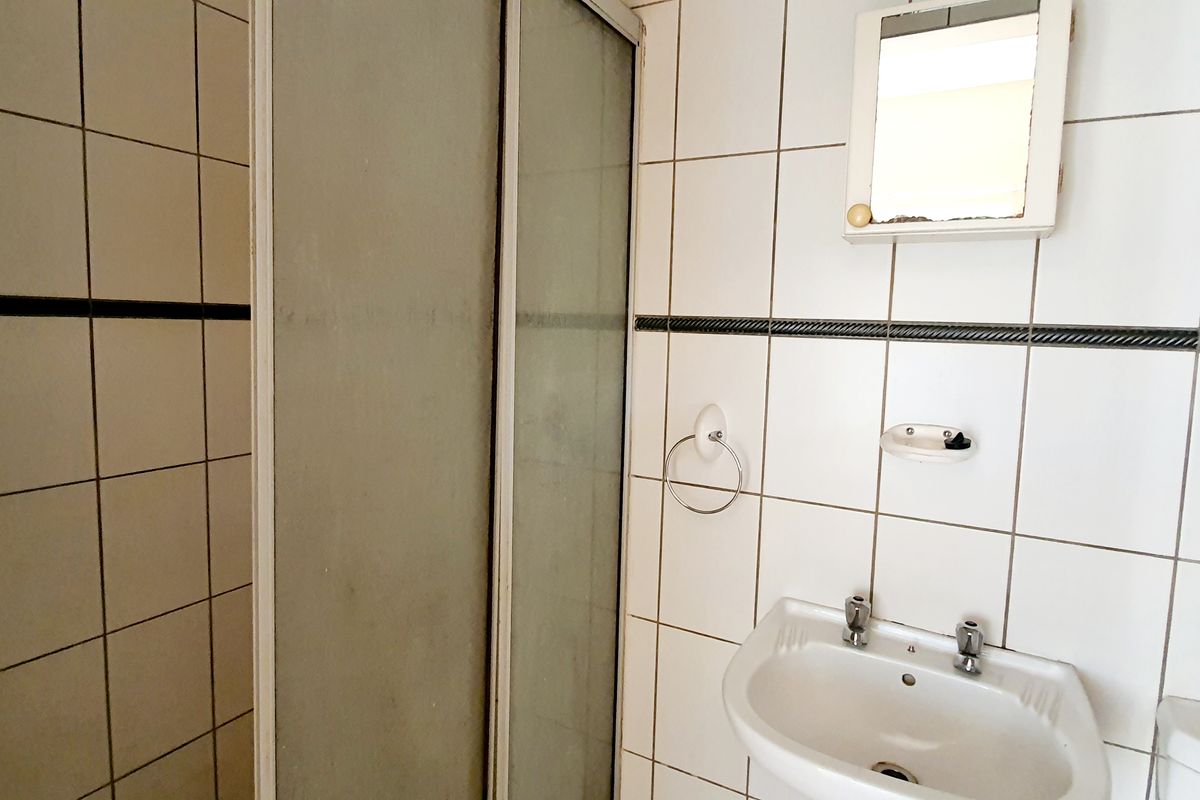 A compact bathroom featuring a shower enclosure, wall-mounted basin, and tiled walls. The space shows signs of age and requires cosmetic updates.