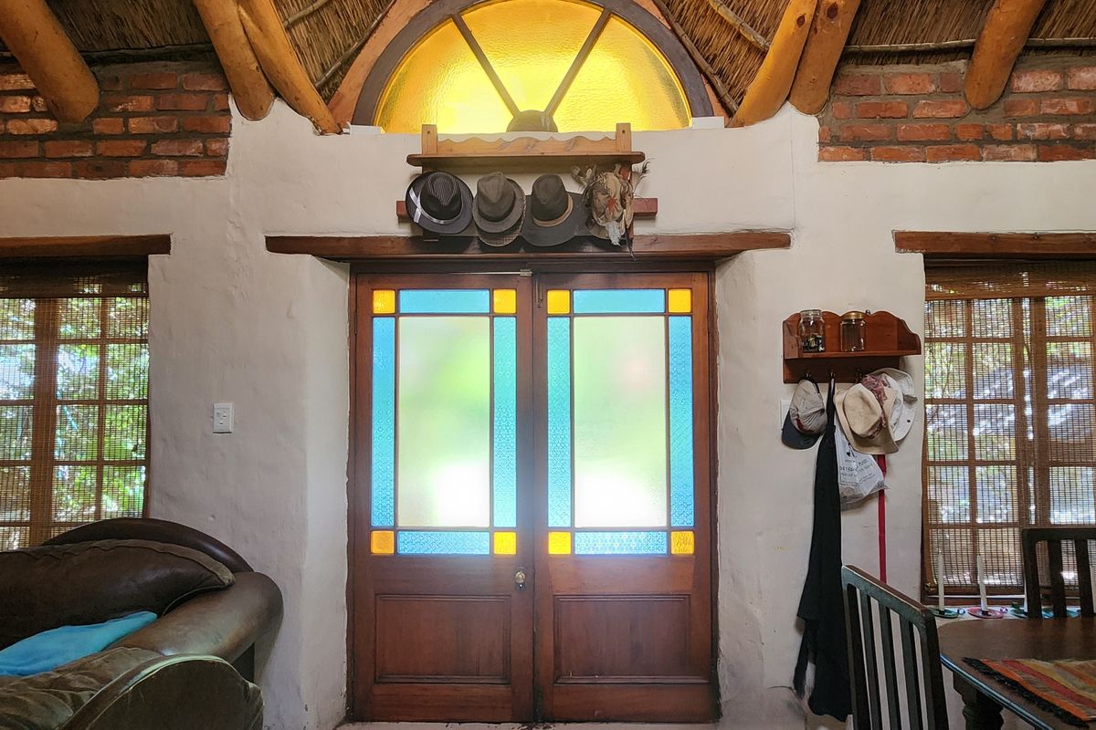 Living area featuring rustic exposed brick walls, a thatched ceiling with timber rafters, and distinctive stained glass double doors with an arched transom window.