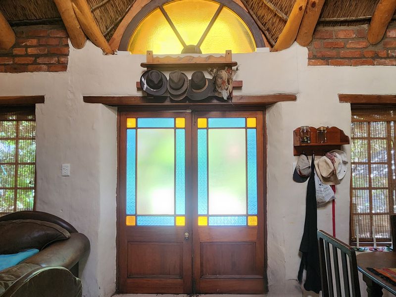 Living area featuring rustic exposed brick walls, a thatched ceiling with timber rafters, and distinctive stained glass double doors with an arched transom window.