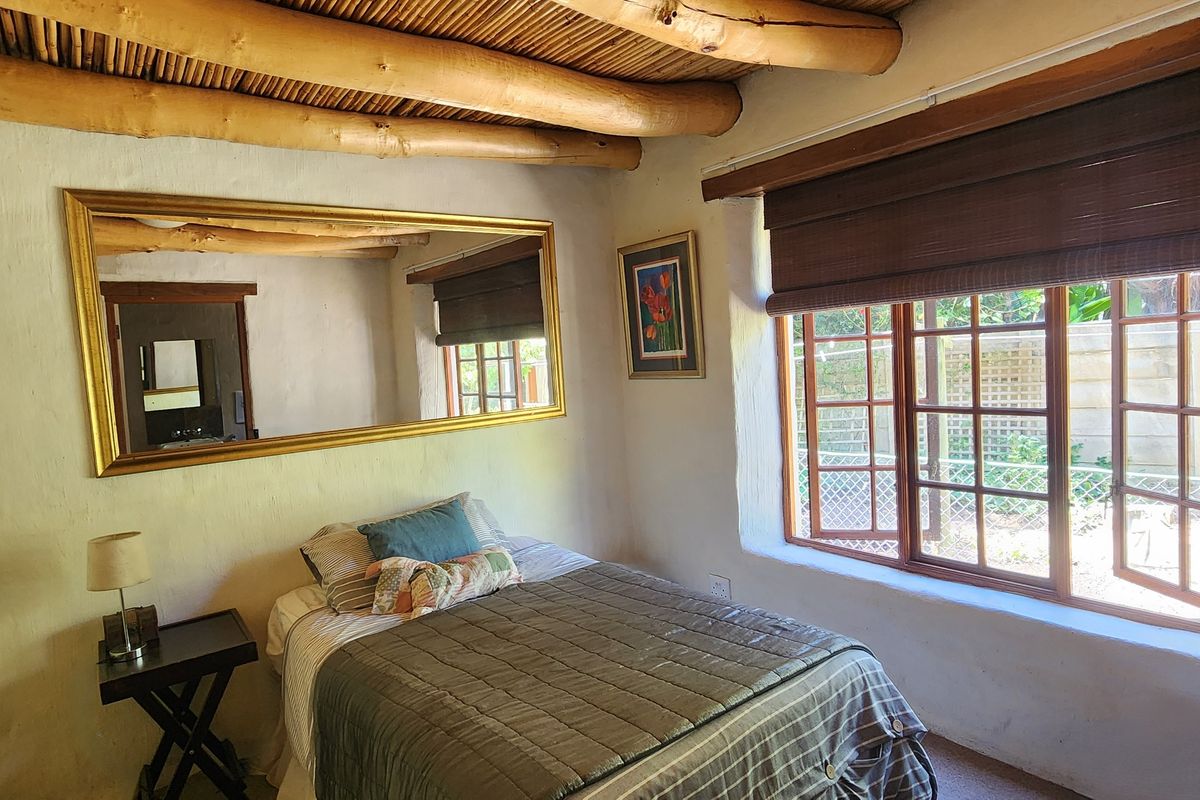 Cozy bedroom featuring a rustic exposed timber beam ceiling, textured plaster walls, and timber casement windows overlooking the garden.