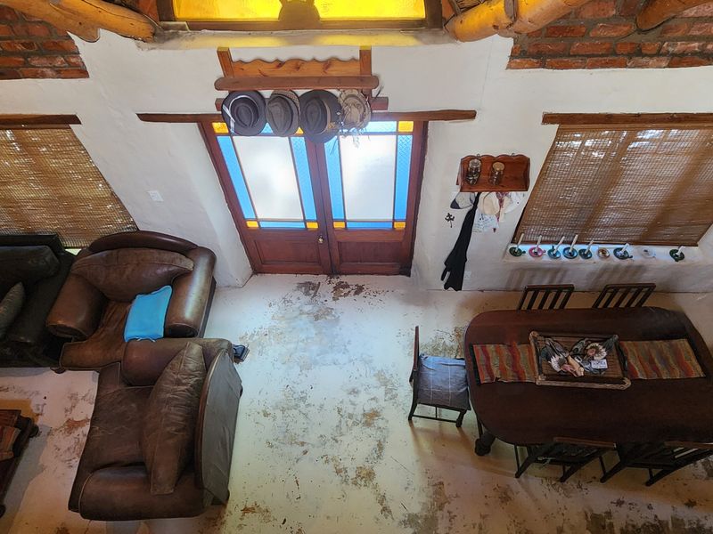 Open plan living and dining area featuring exposed brickwork, timber ceiling beams, stained glass double doors, and rustic concrete flooring.