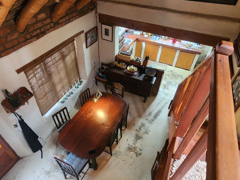 Open plan living and dining area featuring exposed timber rafters, thatched ceiling, exposed brick walls, and a timber staircase leading to the upper level.