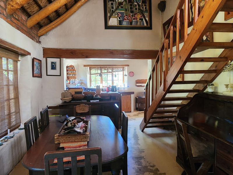 Open-plan living and dining area featuring rustic exposed timber rafters, brickwork, and a wooden staircase leading to an upper level.