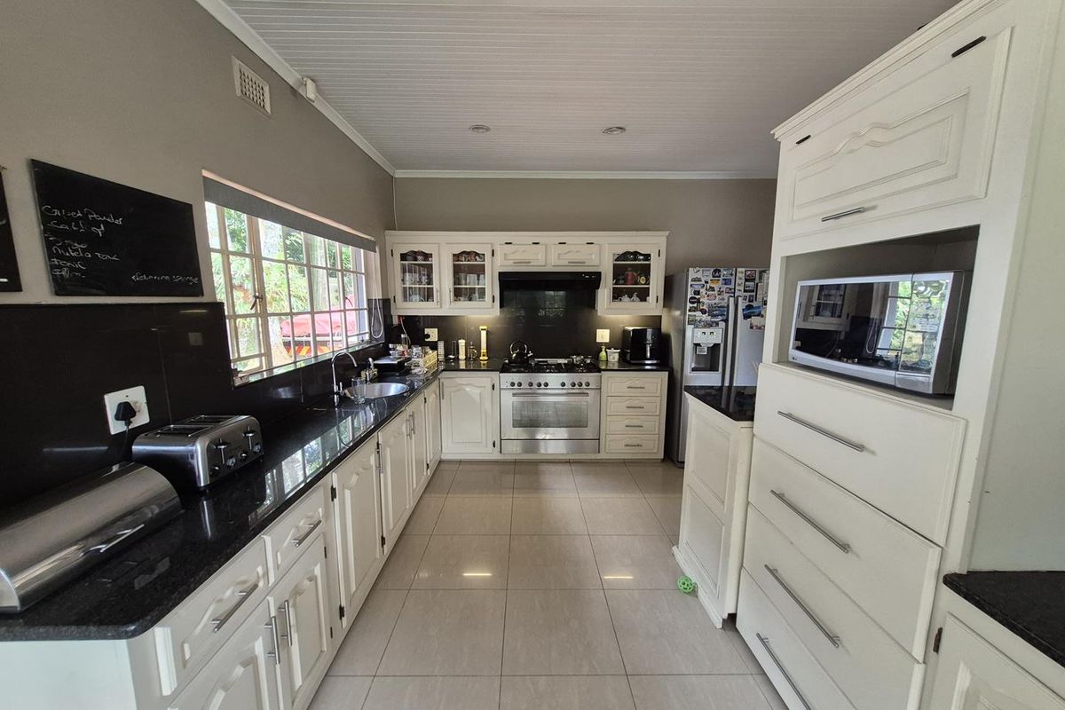 A well-maintained kitchen featuring white cabinetry, black granite countertops, a stainless steel gas stove with extractor fan, and tiled flooring.
