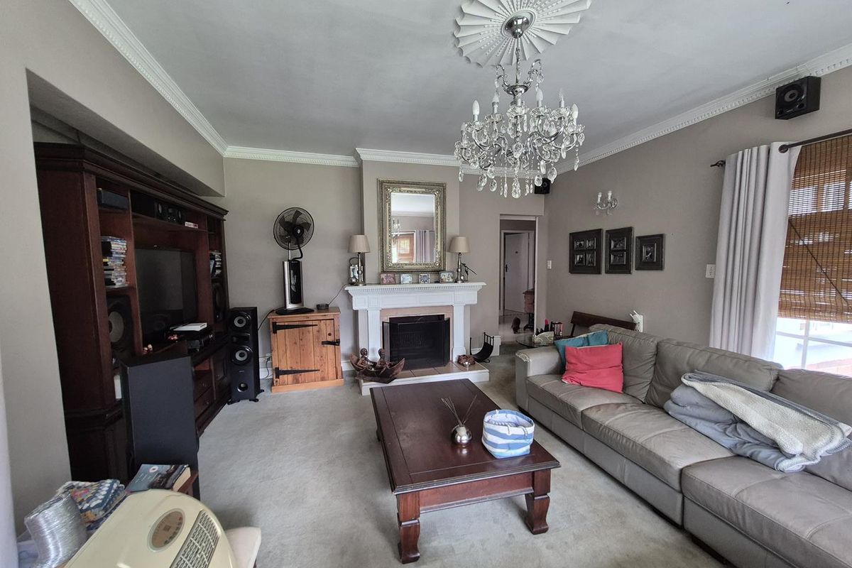 A traditional living room featuring a central fireplace with a decorative mantelpiece, ornate ceiling rose, and crystal chandelier.