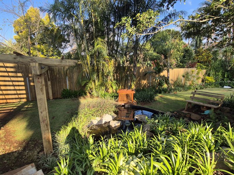 A lush, landscaped rear garden featuring a small decorative pond, timber pergola structure, and established perimeter fencing.