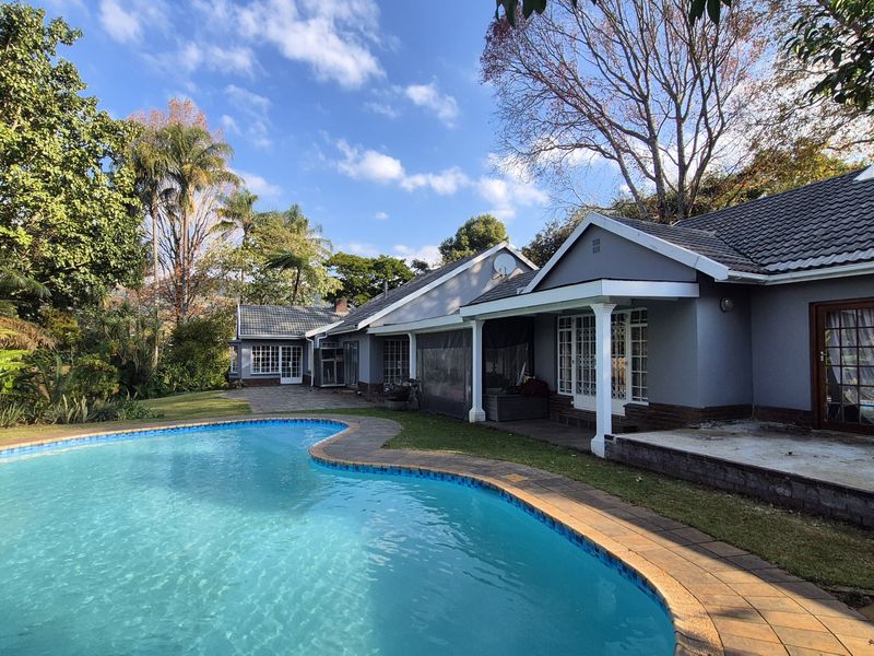 A spacious rear garden featuring a large swimming pool, paved surround, and a covered patio area attached to the main house structure.