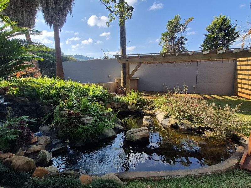 A landscaped garden featuring a decorative rock pond with water feature and a wooden pergola structure.