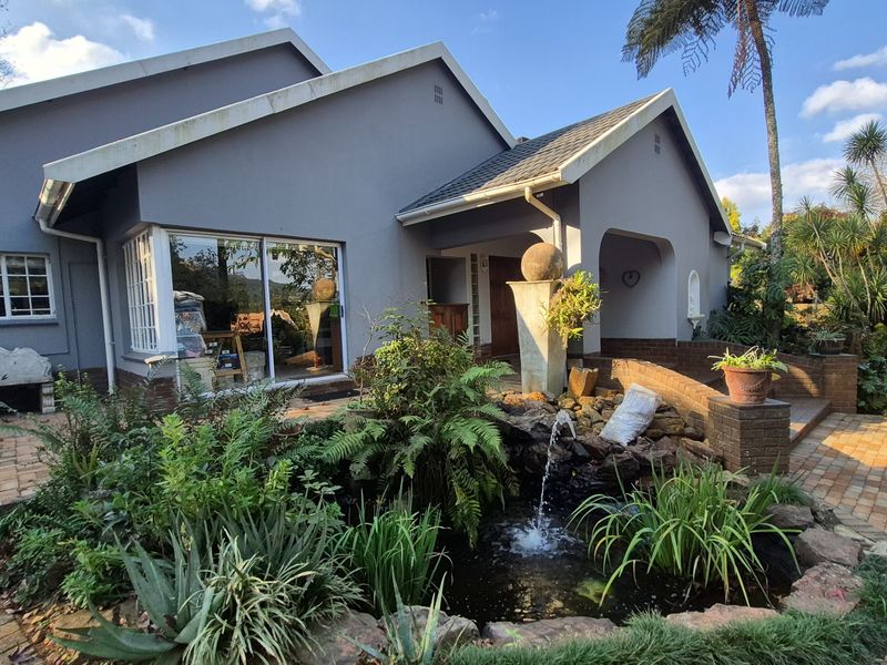 A charming rear exterior view featuring a landscaped garden with a decorative water feature, brick paving, and a covered patio area.
