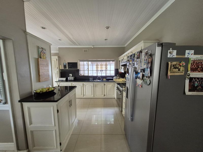A functional kitchen featuring white cabinetry, dark granite countertops, tiled flooring, and a tongue-and-groove ceiling, offering a classic and practical layout.