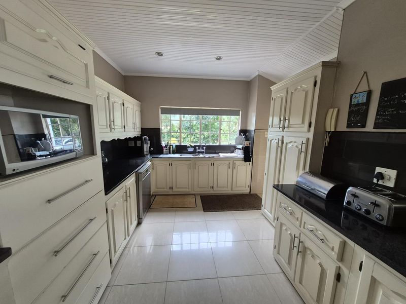 A functional kitchen featuring cream-colored cabinetry, dark granite countertops, a double sink, and tiled flooring with a built-in microwave and integrated storage.