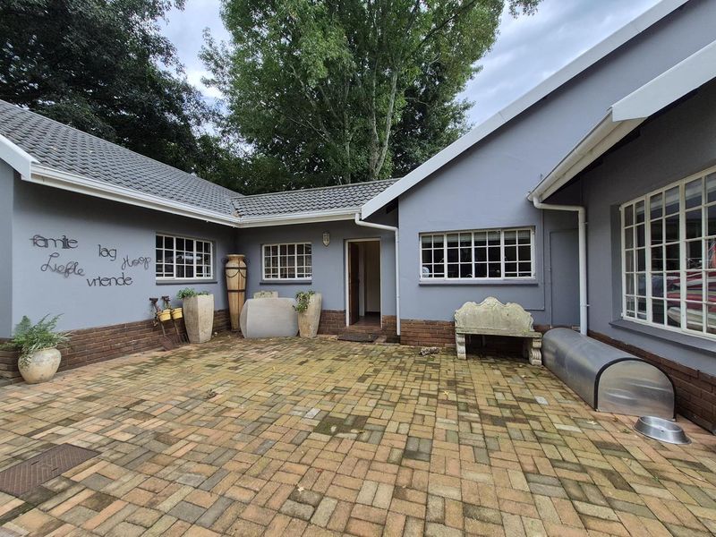 A paved rear courtyard area featuring grey painted exterior walls, brick base detailing, and multiple windows providing access to the home.