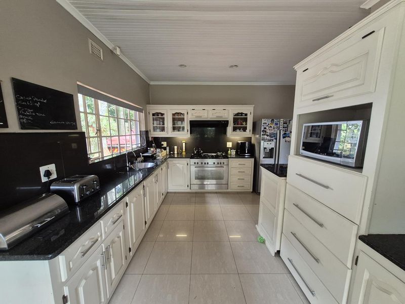 A well-maintained kitchen featuring white cabinetry, black granite countertops, a stainless steel gas stove with extractor fan, and tiled flooring.