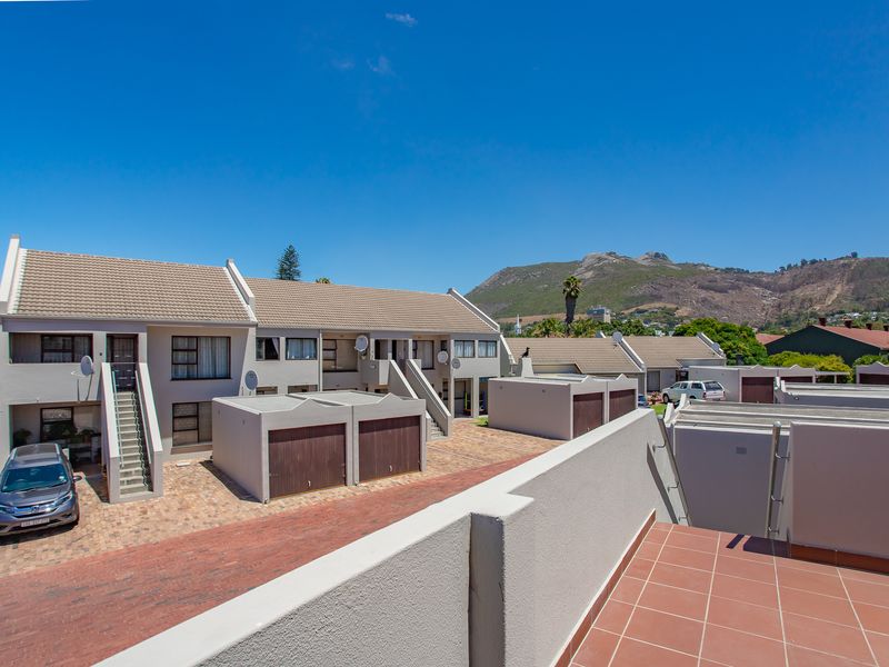 Exterior view of an apartment complex featuring paved driveways, individual garage units, and external staircases against a mountain backdrop.