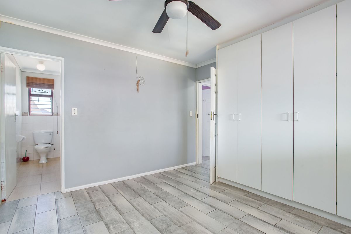 A bright, empty bedroom featuring modern grey tiled flooring, built-in white cupboards, and a ceiling fan, with an adjoining bathroom visible.