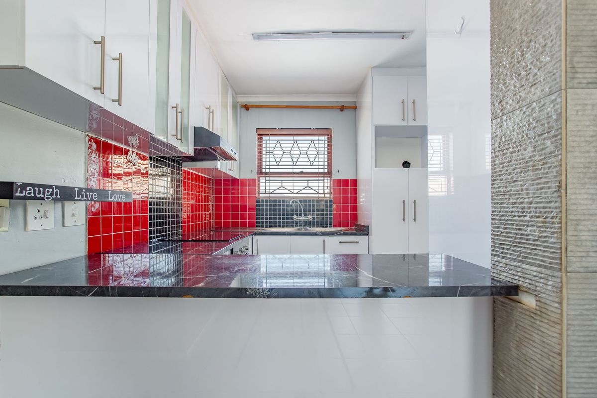 A functional kitchen featuring white cabinetry, dark stone countertops, and a vibrant red and black tiled splashback with a window for natural light.