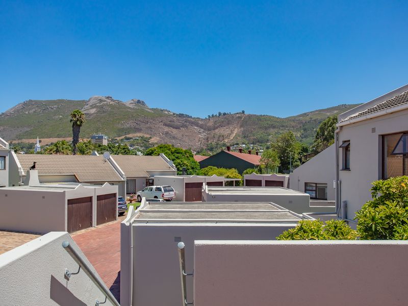 An elevated view of the apartment complex exterior, featuring paved driveways, garage units, and scenic mountain views in the background.