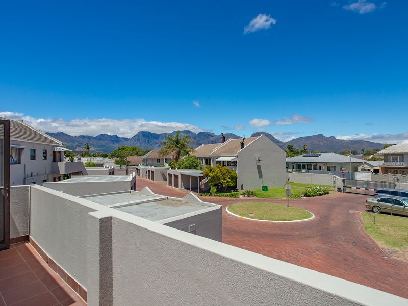 A spacious balcony with tiled flooring and a parapet wall, offering expansive views of the surrounding residential complex and distant mountain range.