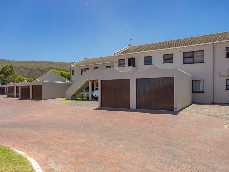 Front exterior view of a multi-unit apartment complex featuring brick paved driveways, individual garage doors, and a tiled roof structure.