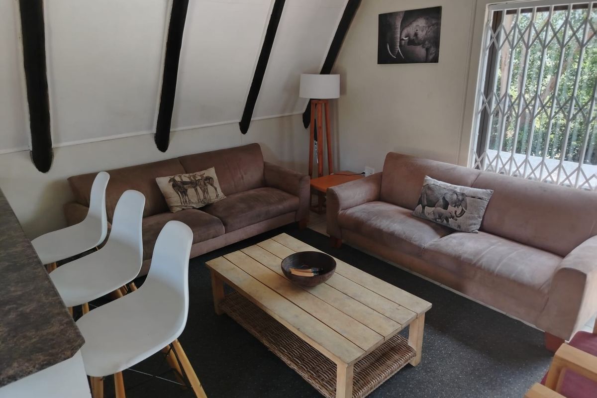A cozy living area featuring exposed timber rafters, a breakfast bar, and a security gate leading to the exterior.