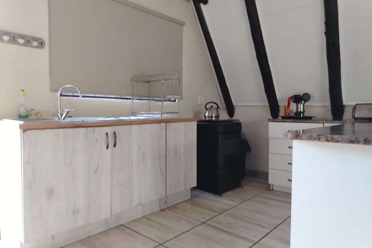A compact kitchen featuring light wood-finish cabinetry, tiled flooring, and exposed timber beams, creating a rustic yet functional cooking space.