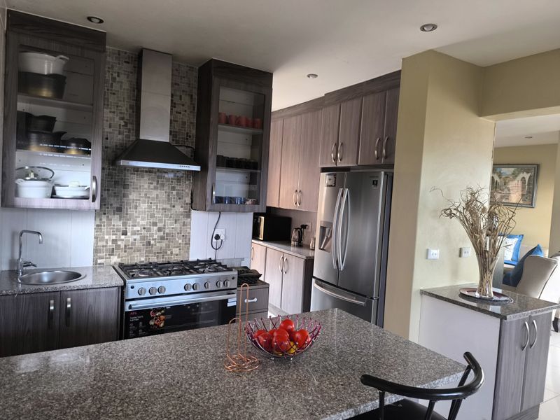 Modern kitchen featuring granite countertops, gas stove with extractor fan, mosaic tile backsplash, and ample built-in cabinetry with a central island.