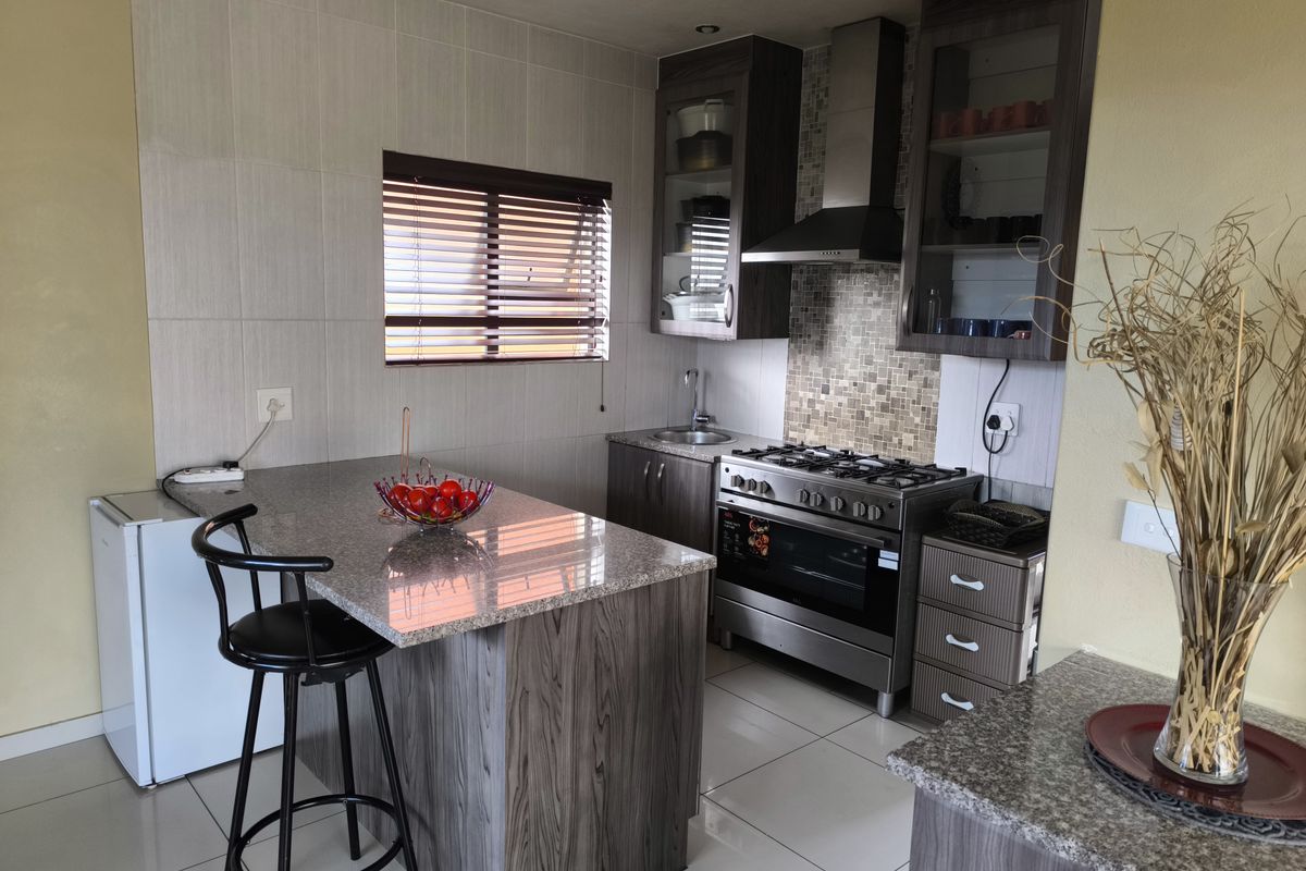 Modern kitchen featuring granite countertops, gas stove with extractor fan, tiled backsplash, and ample built-in cabinetry with a breakfast bar island.