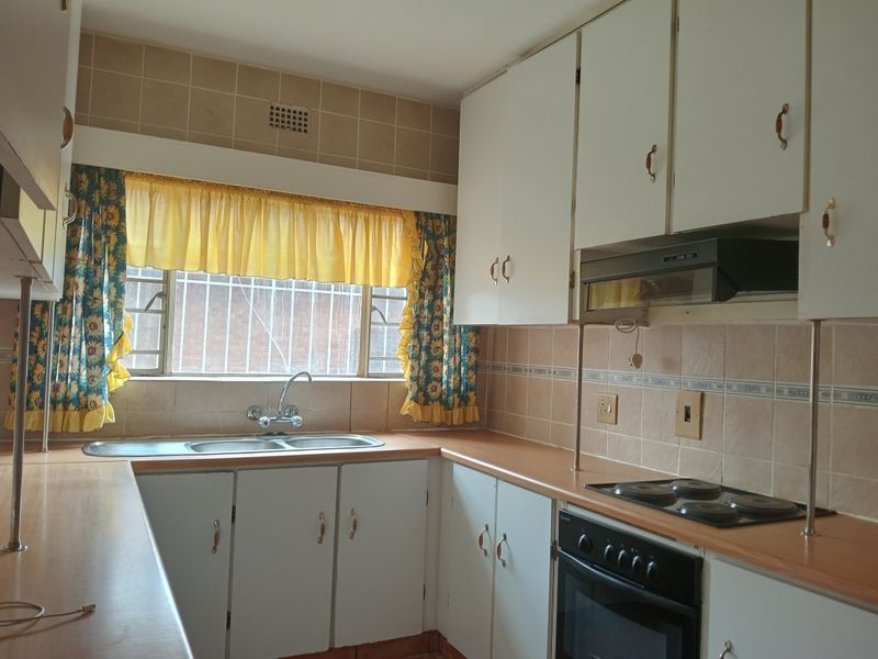 A functional kitchen featuring built-in cabinetry, laminate countertops, a double sink, and integrated electric cooking appliances with a tiled backsplash.