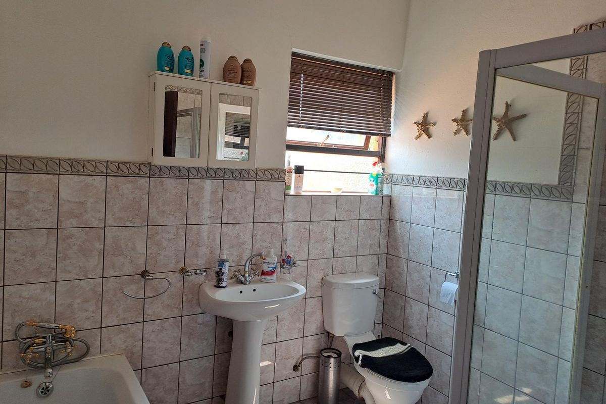 A functional bathroom featuring a pedestal basin, toilet, bathtub, and a separate shower enclosure with tiled walls and a window.