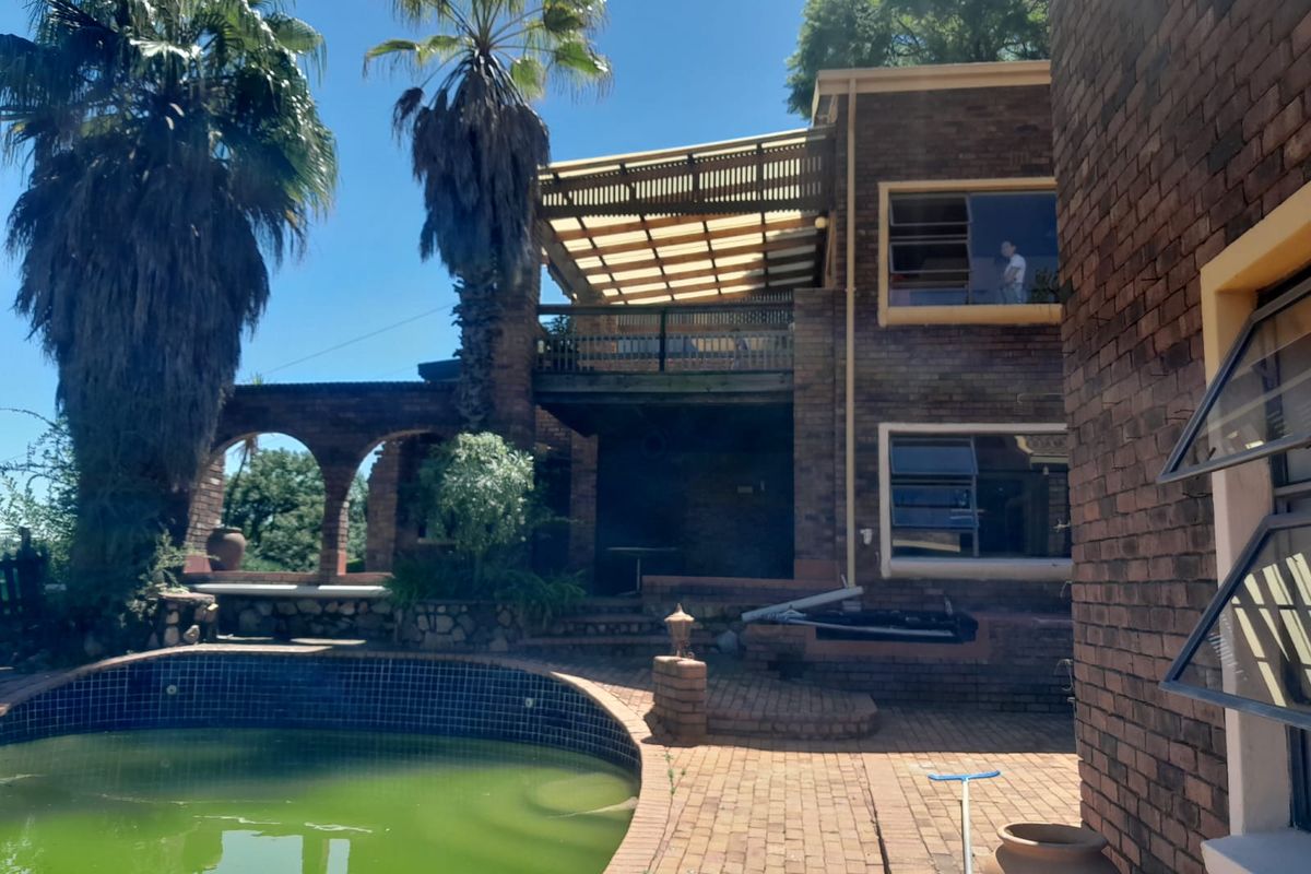 Rear exterior view featuring a brick facade, swimming pool, and elevated balcony with a covered patio area.