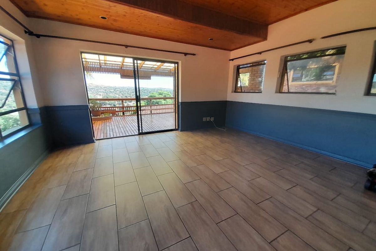 Spacious living area featuring wood-paneled ceilings, modern wood-look floor tiles, and large sliding doors opening onto an outdoor deck with scenic views.