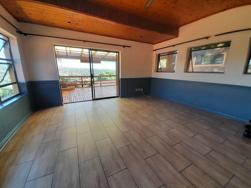 Spacious living area featuring wood-paneled ceilings, modern wood-look floor tiles, and large sliding doors opening onto an outdoor deck with scenic views.