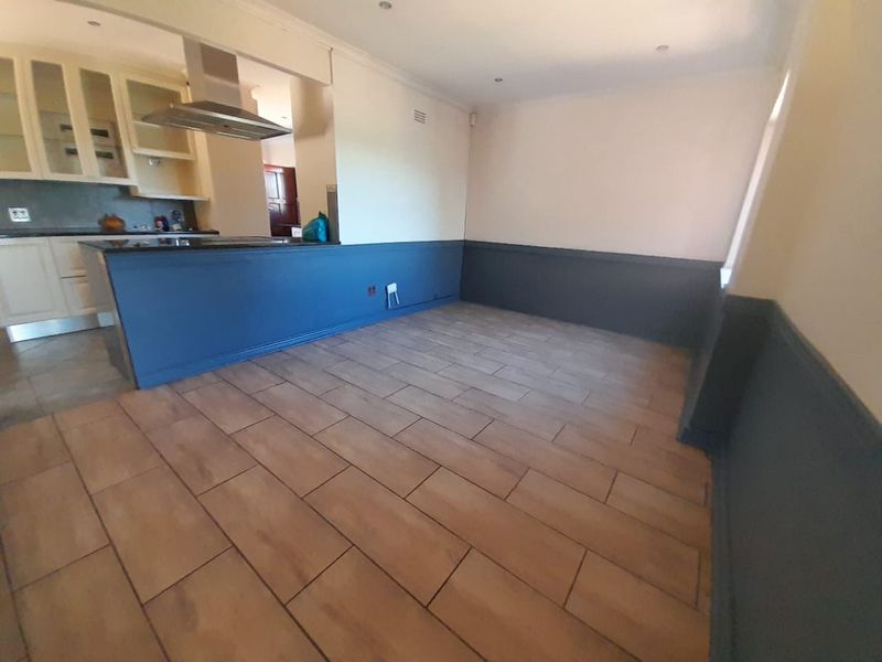 An open-plan living and kitchen area featuring tiled flooring, wainscoting, and built-in kitchen cabinetry with an overhead extractor fan.