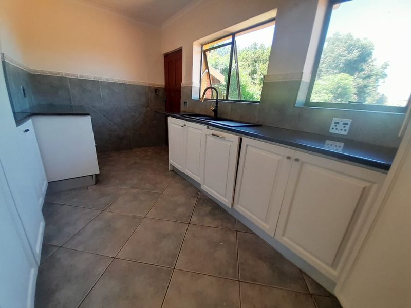 A clean, empty kitchen featuring white cabinetry, dark stone countertops, a double sink with a modern mixer tap, and neutral tiled flooring.