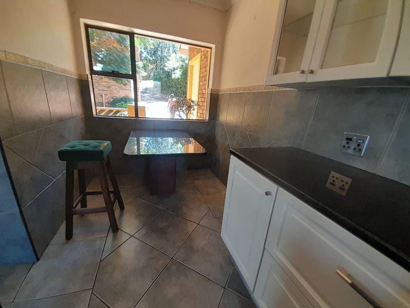 A functional kitchen area featuring built-in white cabinetry, dark stone countertops, and tiled finishes throughout, with a window providing natural light.