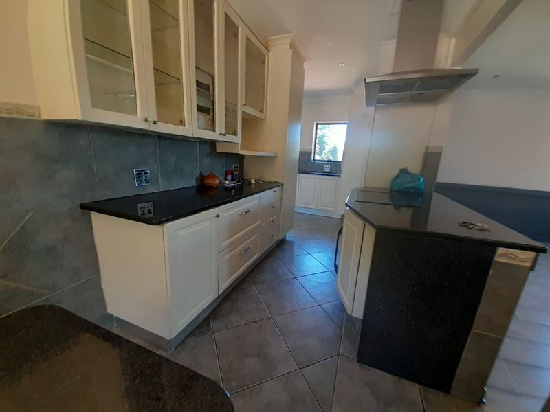 A functional kitchen featuring granite countertops, ample built-in cabinetry, a stainless steel extractor fan, and tiled flooring, with a secondary prep area visible.
