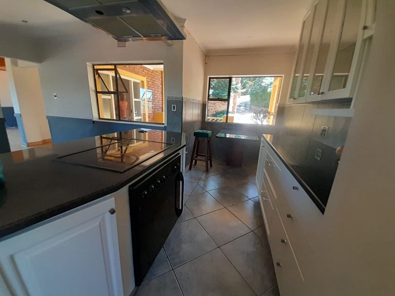 A functional kitchen featuring white cabinetry, dark granite countertops, a built-in hob with extractor fan, and tiled flooring with natural light.