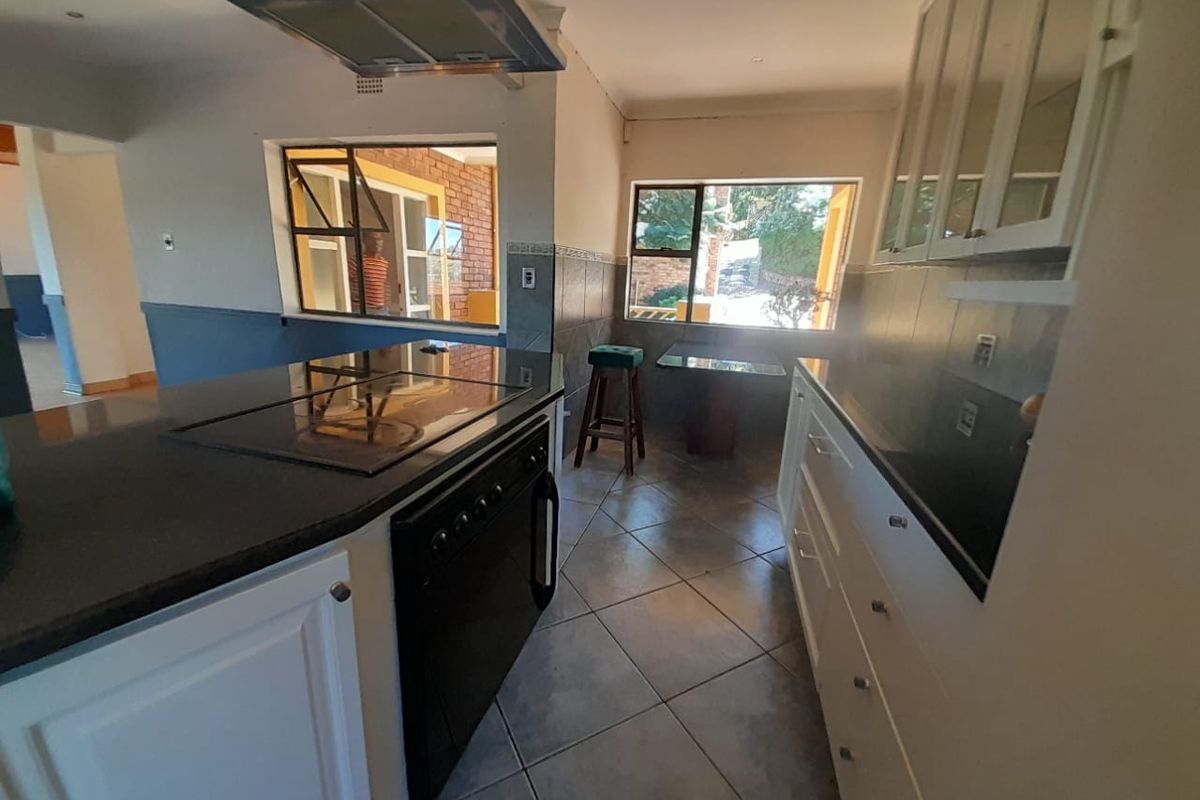 A functional kitchen featuring white cabinetry, dark granite countertops, a built-in hob with extractor fan, and tiled flooring with natural light.