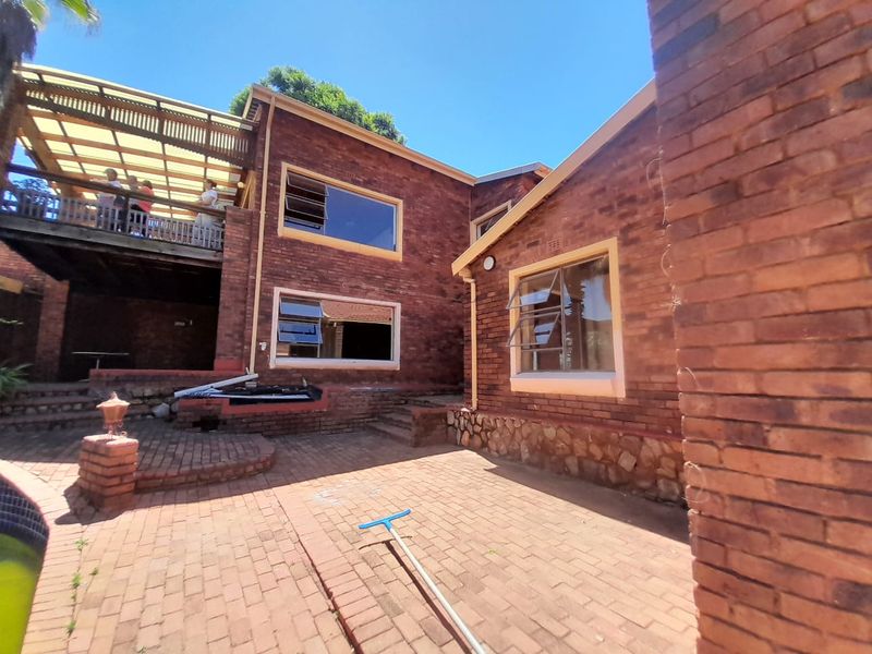 Rear view of a face-brick house featuring a raised wooden deck with a pergola and a paved patio area.