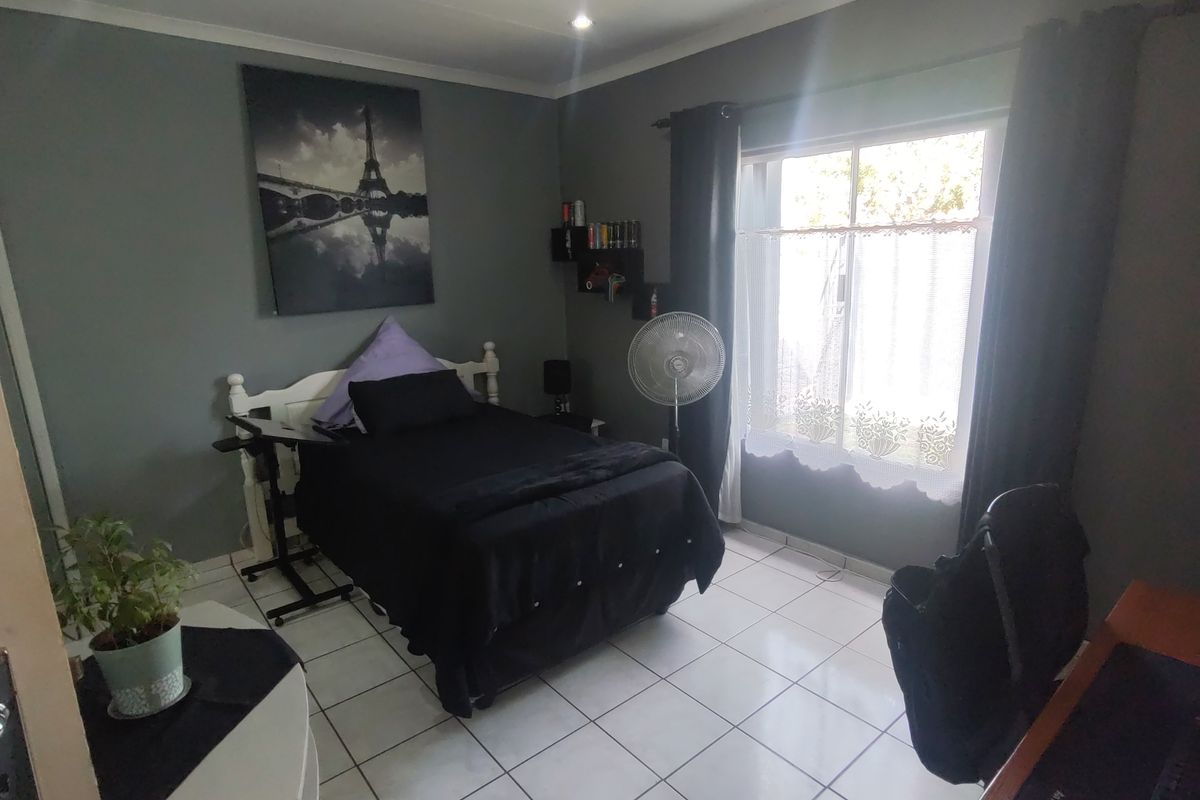 A functional bedroom featuring tiled flooring, recessed lighting, and a sliding window, providing a comfortable space with neutral wall tones.