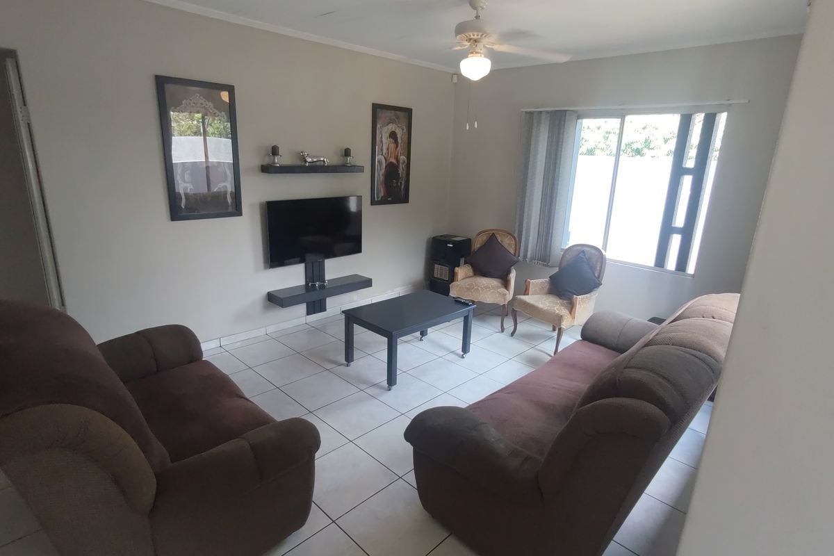 A functional living room featuring tiled flooring, a ceiling fan, and wall-mounted shelving, providing a comfortable and practical space for relaxation.