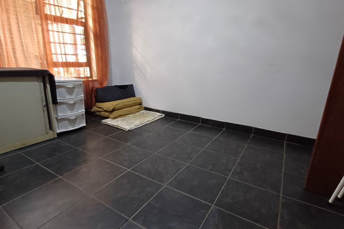 A simple bedroom featuring dark tiled flooring and a window fitted with security bars, offering a blank canvas for personalization.