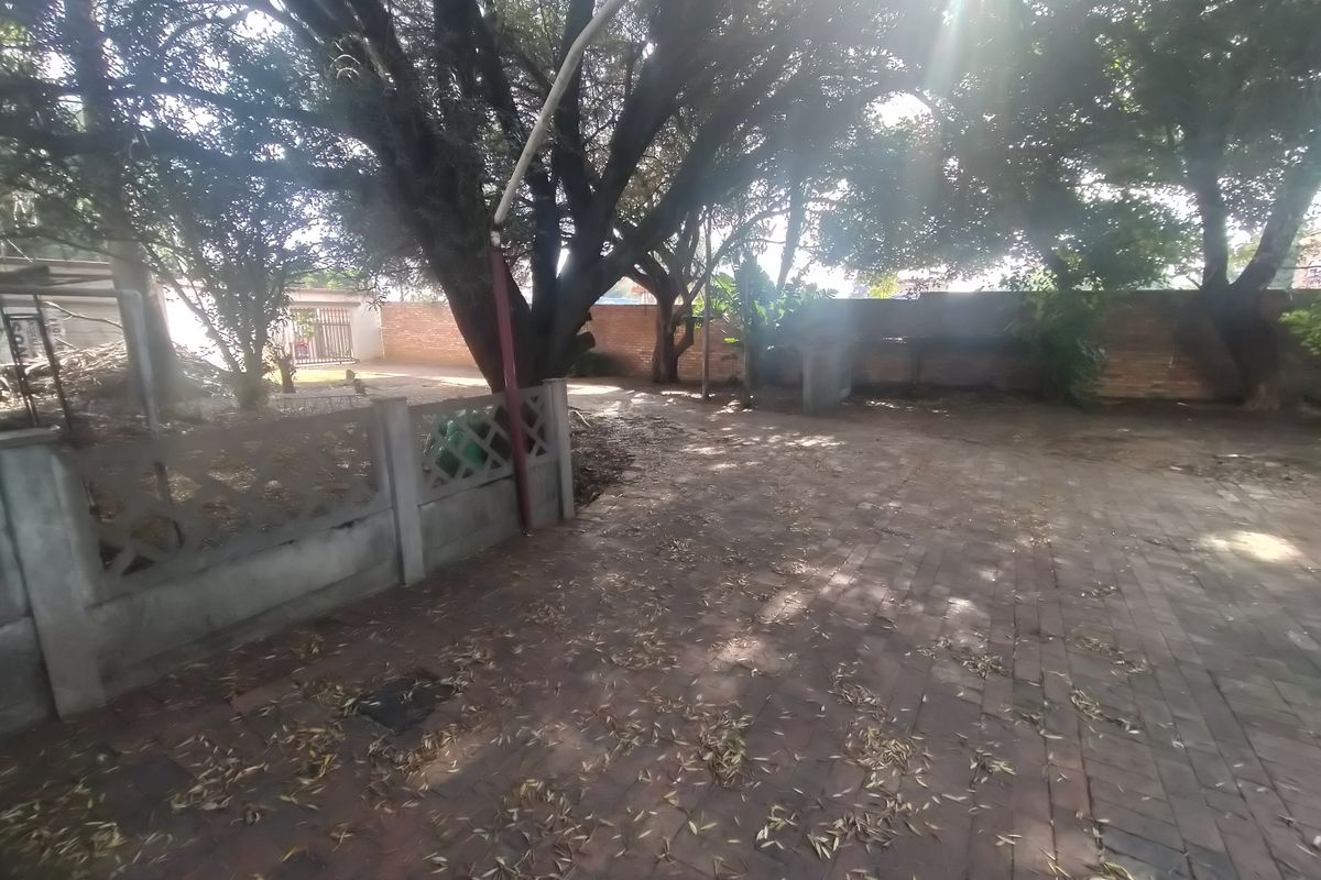 A rear outdoor area featuring brick paving, mature trees, and perimeter walling, providing a private space with potential for landscaping.