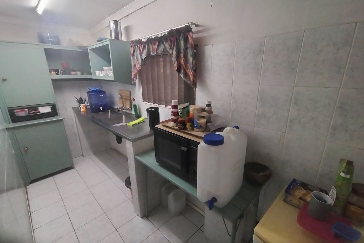 A functional kitchen featuring built-in cabinetry, a stainless steel sink, and tiled splashbacks, offering a dated aesthetic ready for modernization.