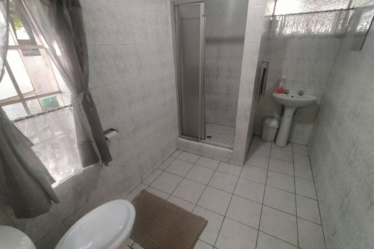 A functional bathroom featuring a shower enclosure, pedestal basin, and toilet with neutral wall and floor tiling.