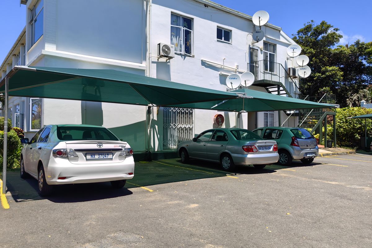 Rear exterior view of the retirement village building featuring a shaded parking area, external staircase, and multiple satellite dish installations.